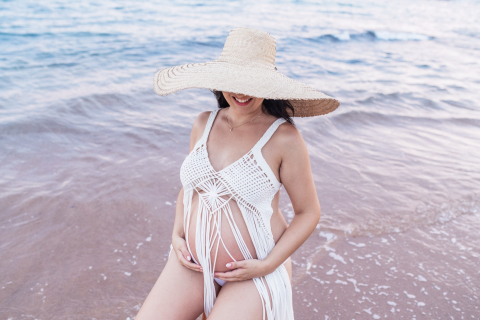 A picture was taken in Mar do Norte, Brazil, showing a pregnant mom alone at the beach kneeling in the shore waters and wearing a big hat.