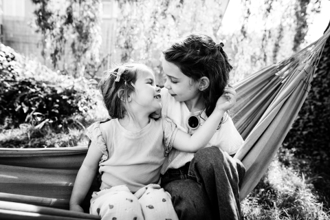 At Arnas in France, a beautiful black and white photo captures two sisters tenderly hugging in a hammock, showing their love and bond in a sweet scene.
